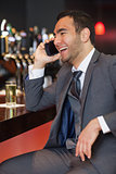 Cheerful businessman on the phone having a drink