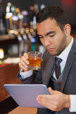 Serious businessman working on his tablet computer while having a whisky
