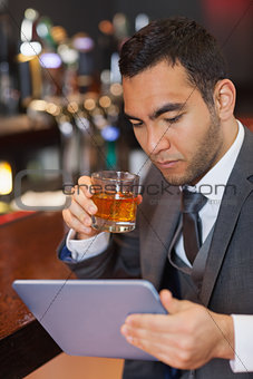 Serious businessman working on his tablet computer while having a whisky