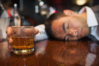 Drunk businessman with whiskey in his hand lying on a counter