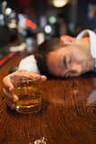 Drunk businessman holding whiskey lying on a counter