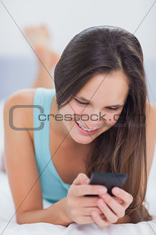 Woman using her phone and smiling while on the bed