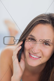 Happy woman lying on bed talking with phone