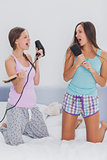 Two girls on bed singing into their hairbrushes
