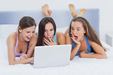Grils on bed looking at laptop