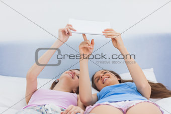 Girls holding tablet and lying in bed