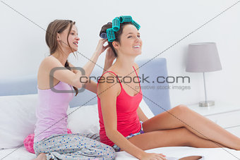 Girls sitting in bed one wearing hair rollers