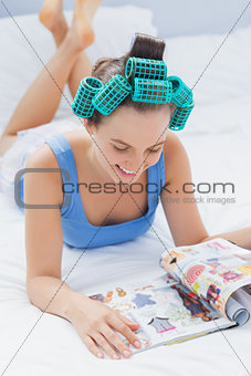 Smiling girl in hair rollers lying on bed
