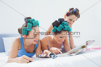 Girls wearing pajamas and hair rollers sitting in bed with magazines