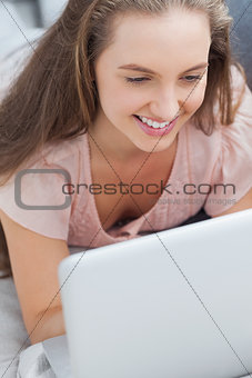 Woman lying on sofa using laptop