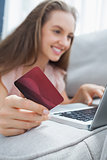Smiling woman lying ona sofa holding a card and laptop