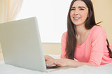 Pretty young girl looking at camera using a laptop lying on a bed