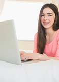 Young girl looking at camera using a laptop lying on a bed