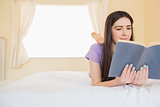 Content girl lying on a bed reading a book