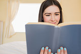 Relaxed girl lying on a bed reading a book