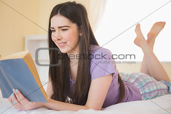 Pretty young girl lying on a bed reading a book