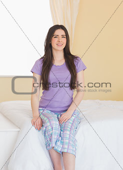 Cheerful girl looking at camera and sitting on a bed