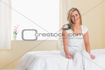 Happy woman looking at camera and sitting on a bed