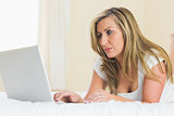 Concentrated woman using her laptop lying on her bed
