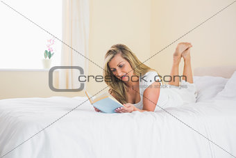 Cheerful woman reading a book lying on her bed