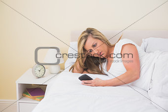 Concentrated woman using a mobile phone lying on her bed