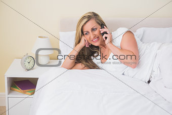 Smiling woman lying on a bed calling someone with her mobile phone
