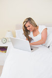 Joyful woman lying on her bed using a laptop