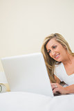Happy woman typing on a laptop lying on her bed
