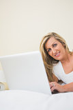 Amused woman typing on a laptop lying on her bed