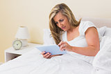 Thoughtful woman using a tablet pc lying on her bed