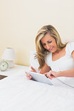 Content woman using a tablet pc lying on her bed