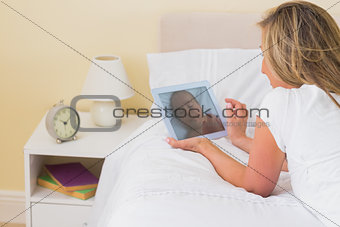 Thoughtful woman using a tablet pc lying on her bed