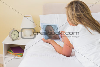 Focused woman using a tablet pc lying on her bed