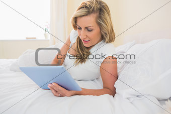 Concentrated woman using a tablet pc lying on her bed
