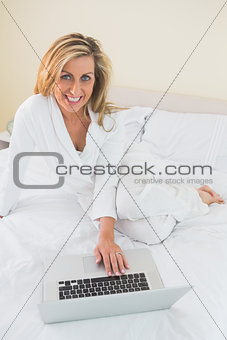 Smiling woman using a laptop lying on her bed