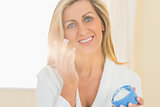 Pleased woman holding a jar of face cream in a hand and applying cream on her chick with the other h