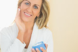 Pleased woman holding a jar of face cream in a hand and applying cream on her chick with the other h