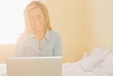 Happy woman sitting on a bed using her laptop