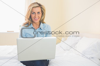 Pleased woman sitting on a bed using her laptop