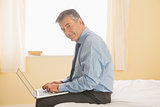 Thoughtful man using a laptop sitting on a bed