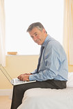 Focused man using a laptop sitting on a bed