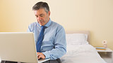 Thoughtfulman using a laptop sitting on a bed