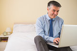 Content man using a laptop sitting on a bed