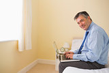 Pleased man using a laptop sitting on a bed