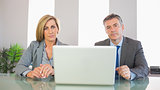 Two severe business people looking at camera behind a laptop