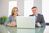 Two smiling business people looking at camera behind a laptop