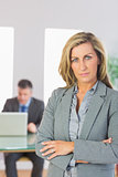 Serious businesswoman looking at camera crossed arms with a businessman working on background