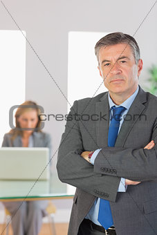 Irritated businessman looking at camera crossed arms with a businesswoman working on background