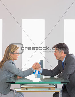 Two content businesspeople having an arm wrestling sitting around a table