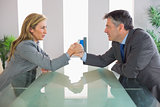 Two irritated businesspeople having an arm wrestling sitting around a table
